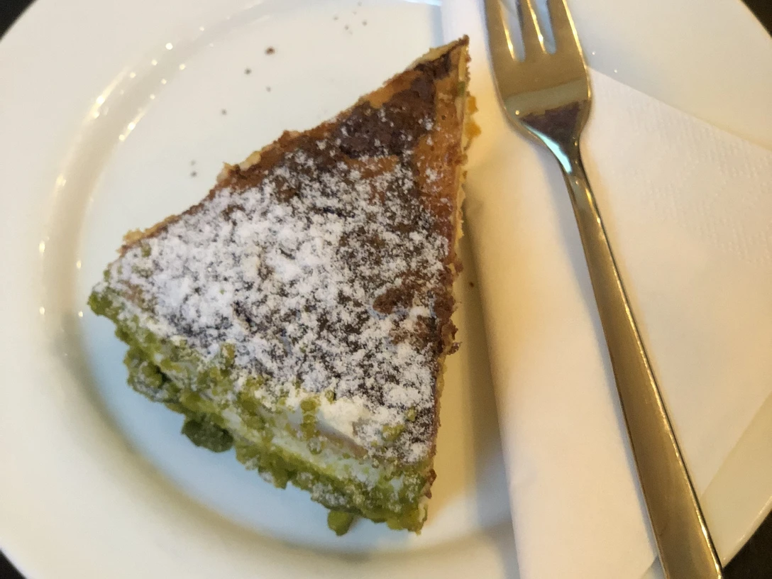Torte Ein Stück Torte mit grüner Füllung und Puderzucker, serviert auf einem weißen Teller mit Gabel.