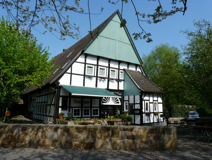 Altes Farmhaus Lienen_Frontansicht_Foto Dierkschneider.jpg Fachwerkhaus in Lienen mit grüner Markise, umgeben von Bäumen und einem gepflasterten Vorplatz.