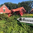 Motorrad- und Puppenmuseum Ein rotes Motorrad steht auf einem grünen Busch vor einem ziegelroten Gebäude mit Museumsschildern.