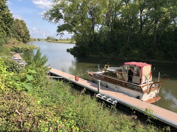 Segelboot an einem ruhigen Steg am Hafen Stolzenau, umgeben von dichter Vegetation und Bäumen.