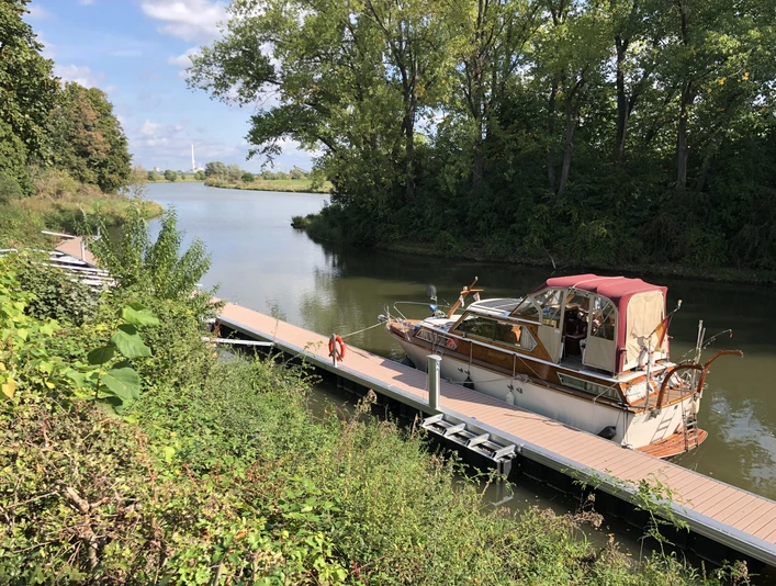 Segelboot an einem ruhigen Steg am Hafen Stolzenau, umgeben von dichter Vegetation und Bäumen.