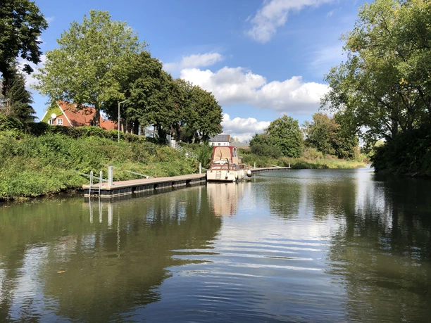 Haus, Bäume und Boot am Wasserlauf unter blauem Himmel mit weißen Wolken in Stolzenau.