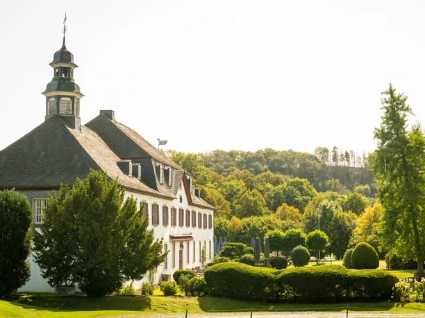 Schloss Auel Historisches Herrenhaus mit gepflegtem Garten und Wald im Hintergrund bei sonnigem Wetter.