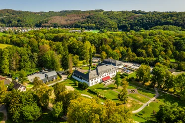 Schloss Auel Luftaufnahme eines historischen Herrenhauses umgeben von dichten Wäldern und gepflegten Grünflächen.