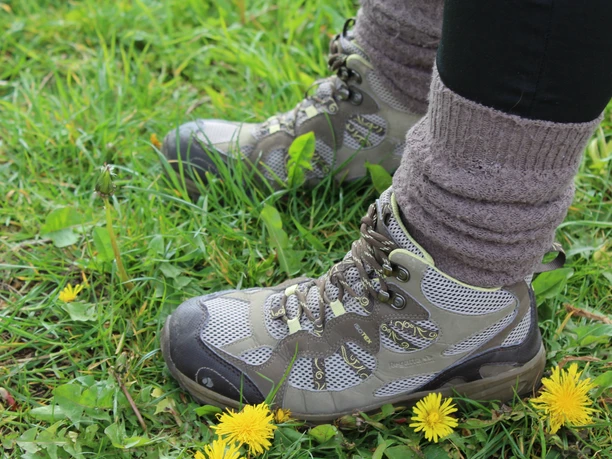 Wandern Robuste Wanderstiefel stehen in lebendig grünem Gras, umgeben von blühendem Löwenzahn.