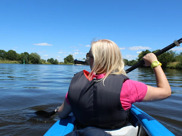 Eine Frau paddelt in einem blauen Kanu auf einem ruhigen Fluss, umgeben von grüner Landschaft.