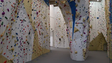 2T-Kletterhalle Lindlar Kletterhalle mit bunten Griffen und hohen Wänden, eine Person ist beim Klettern zu sehen.