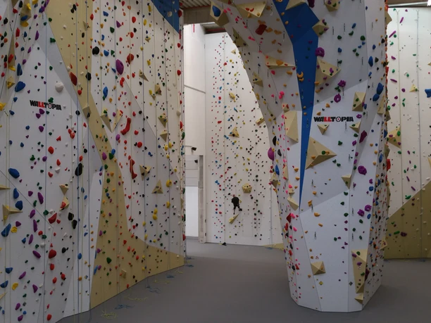 2T-Kletterhalle Lindlar Kletterhalle mit bunten Griffen und hohen Wänden, eine Person ist beim Klettern zu sehen.