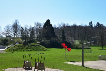 Spielplatz im Freizeitpark <p>Grüne Parklandschaft mit Hügeln, Skatepark und rotem Basketballkorb unter klarem Himmel.</p>
