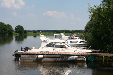 Ein ruhiger Campingplatz an einem von Booten gesäumten Flussufer mit üppigem Grün und klarem Himmel.
