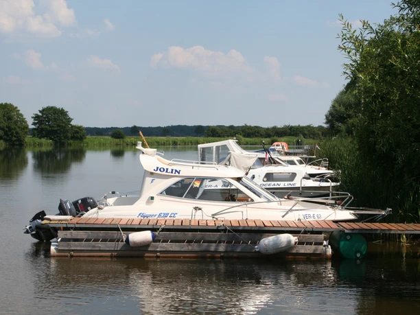 Ein ruhiger Campingplatz an einem von Booten gesäumten Flussufer mit üppigem Grün und klarem Himmel.