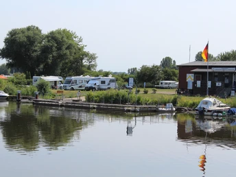 Ruhige Flussuferlandschaft mit Wohnmobilen und Bootsanlegestelle auf Campingplatz in Drakenburg.