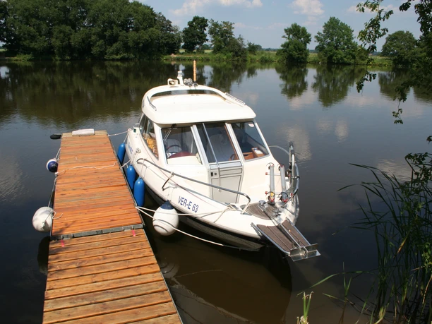 Motorboot an einem Holzsteg, umgeben von ruhigem Wasser und grüner Natur im Campingplatz Drakenburg.