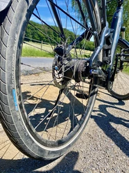 Fahrradreifen Beispielbild Nahaufnahme eines Fahrradhinterrads auf einem Radweg, mit grünem Hügel und blauem Himmel im Hintergrund.