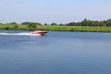 Ein schnelles Motorboot gleitet über die ruhige Weser, umgeben von grüner Landschaft und blauem Himmel.