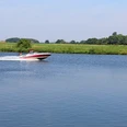 Dörverden Weser Ein schnelles Motorboot gleitet über die ruhige Weser, umgeben von grüner Landschaft und blauem Himmel.