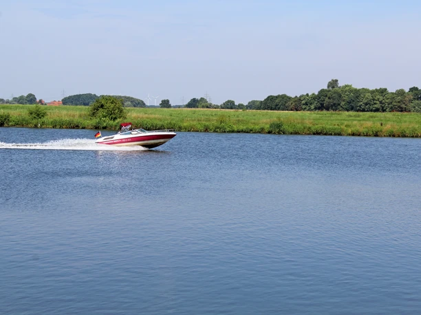 Dörverden Weser Ein schnelles Motorboot gleitet über die ruhige Weser, umgeben von grüner Landschaft und blauem Himmel.