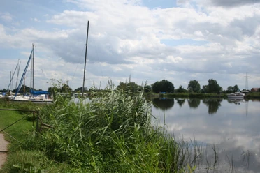 Eine ruhige Flusslandschaft mit mehreren vertäuten Segelbooten am Ufer und bewölktem Himmel.