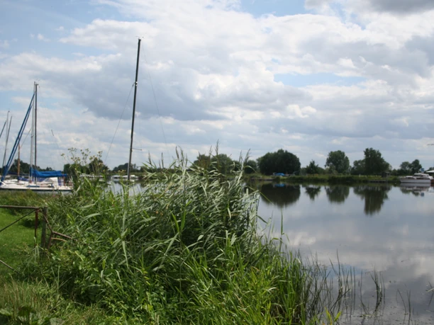 Eine ruhige Flusslandschaft mit mehreren vertäuten Segelbooten am Ufer und bewölktem Himmel.