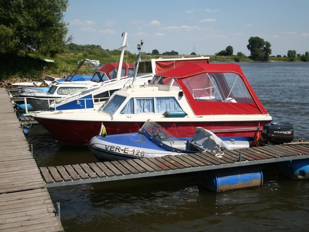 A river dock with reddish boats under a blue sky, including a small motorboat.