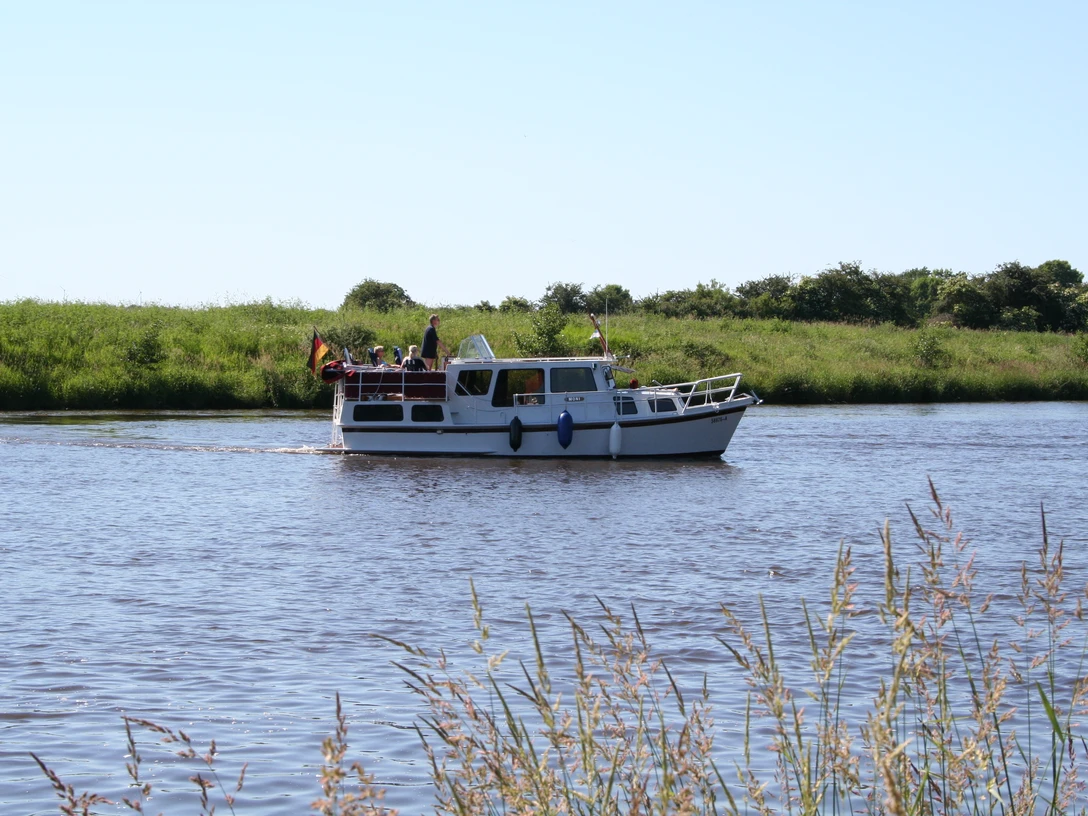 Boot auf Mittelweser Ein kleines Motorboot mit Personen fährt entlang eines ruhigen Flusses, umgeben von grüner Natur.
