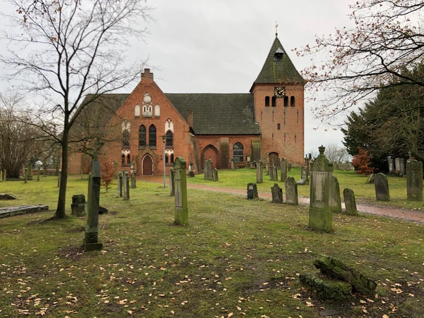 Bakstenen kerk van Daverden met karakteristieke toren, omringd door historische grafstenen.