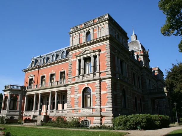De foto toont het majestueuze kasteel Etelsen in rode baksteen met prachtige decoraties onder een blauwe hemel.