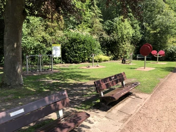 Grüne Wiesen mit Fitnessgeräten und Sitzbänken im Kurpark Bruchhausen-Vilsen an einem sonnigen Tag.