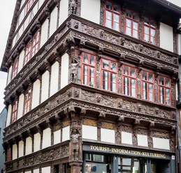 Verziertes historisches Fachwerkhaus mit geschnitzten Figuren, roten Fenstern und Tourist-Info.