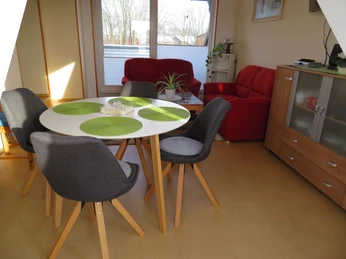 Essecke in Ferienwohnung Schünemann Heller Essbereich in Ferienwohnung mit rundem Tisch, modernen Stühlen und rotem Sofa im Hintergrund.