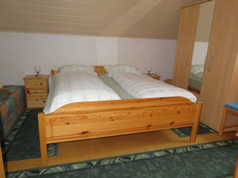 Schlafraum in der Ferienwohnung Schünemann Doppelbett aus Holz mit weißer Bettwäsche, flankiert von zwei Nachttischen mit Lampen.