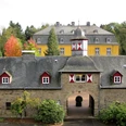 Schloss Heiligenhoven Historisches Schloss mit gelber Fassade, grauem Dach und buntem Herbstlaub im Hintergrund.