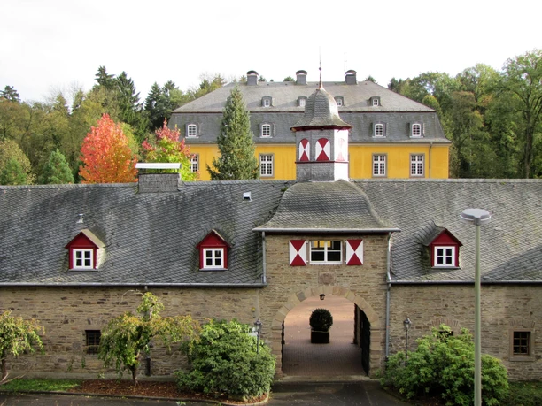 Schloss Heiligenhoven Historisches Schloss mit gelber Fassade, grauem Dach und buntem Herbstlaub im Hintergrund.