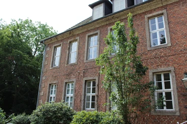 Amtshof 2 Bruchhausen-Vilsen Roter Backsteinbau mit großen weißen Fenstern, umrahmt von üppigem Grün, unter blauem Himmel.