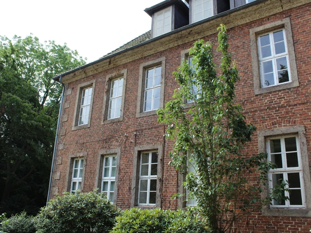 Amtshof 2 Bruchhausen-Vilsen Roter Backsteinbau mit großen weißen Fenstern, umrahmt von üppigem Grün, unter blauem Himmel.