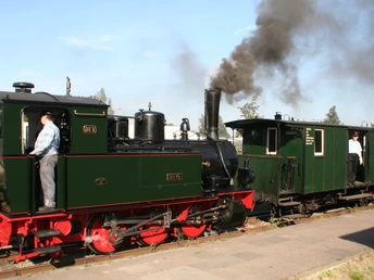 Dampflok zieht historischen Zug auf Schmalspurbahn, zwei Eisenbahnliebhaber stehen auf Plattformen.Steam locomotive pulls historic train on narrow-gauge railroad, two railroad enthusiasts stand on platforms.Damplokomotivet trækker et historisk tog på en smalsporet jernbane, to jernbaneentusiaster står på perronen.Stoomlocomotief trekt historische trein op smalspoor, twee spoorwegliefhebbers staan op perrons.