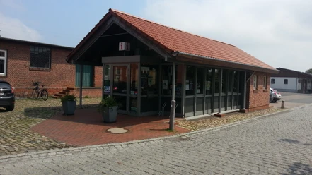 Bakstenen gebouw van één verdieping met rode bakstenen, glazen gevel en informatiebord aan de straat.