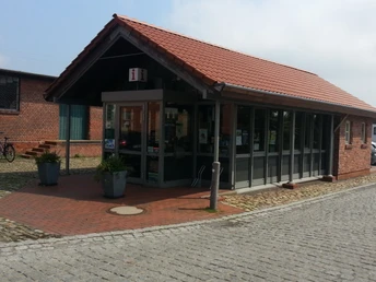 Einstöckiges Backsteingebäude mit roten Ziegeln, Glasfassade und Informationsschild an der Straße.One-storey brick building with red bricks, glass façade and information sign on the street.Murstensbygning i én etage med røde mursten, glasfacade og informationsskilt på gaden.Bakstenen gebouw van één verdieping met rode bakstenen, glazen gevel en informatiebord aan de straat.