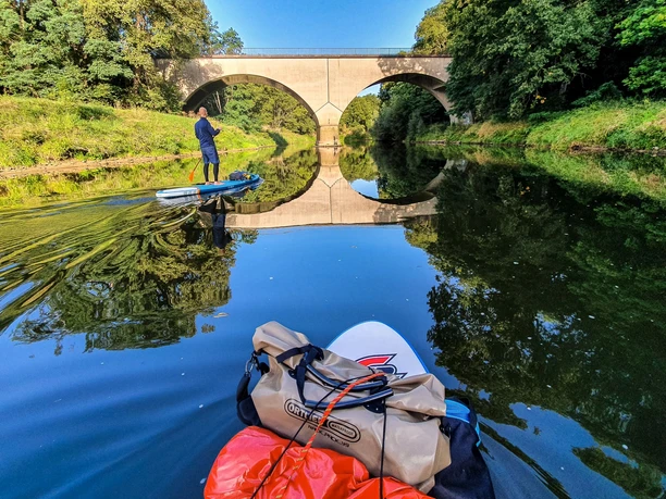 SUP in Rheine an der Ems Brücke Zwei Personen paddeln auf SUP-Boards unter einer steinernen Bogenbrücke auf einem ruhigen Fluss.