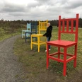 Bunte Riesenstühle auf einem Feldweg, Frau in Winterkleidung steht neben einem roten Stuhl.