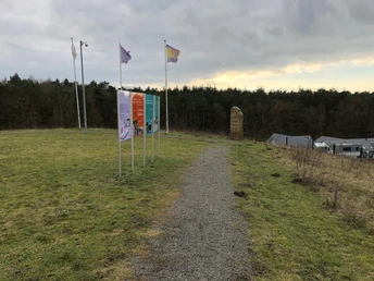 Kräher Höhe Fünf bunte Tafeln informieren auf einem Hügel in einer grünen Landschaft; Bäume im Hintergrund.