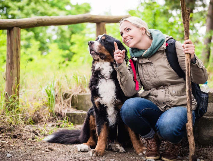 Hiking woman with rucksack and her bernese mountain dog on a trail