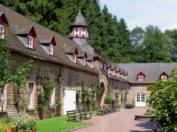 Schloss Heiligenhoven Nebengebäude Historisches Gebäude mit Zinnen und Turm, umgeben von Bäumen und Sitzbänken im Hof.