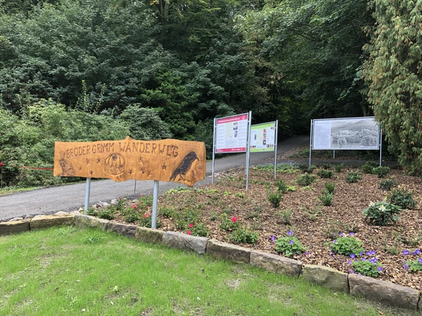 Start Promenadenweg Entrance to the Brothers Grimm Hiking Trail with wooden sign and information boards against a wooded backdrop.