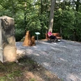 Eine Frau sitzt entspannt auf einer Bank in einem schattigen Wald, neben einer Holzskulptur.