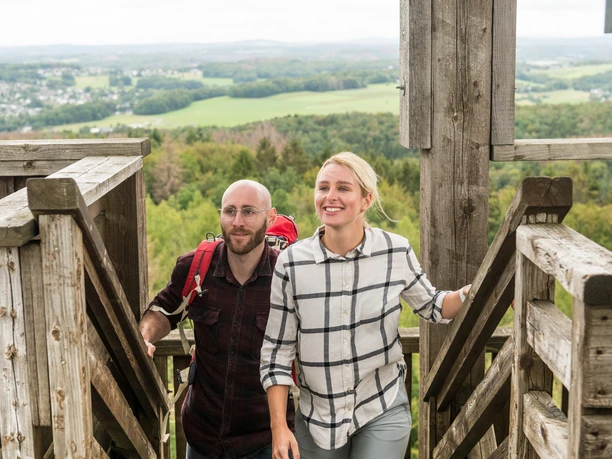 Nümbrecht Zwei Menschen steigen eine hölzerne Treppe hinauf, im Hintergrund eine weite, grüne Landschaft.