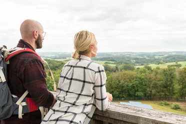 Nümbrecht Paar genießt Panoramaausblick von hölzerner Plattform auf grüne Landschaft unter wolkigem Himmel.