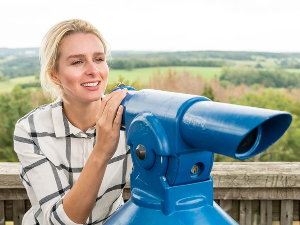 Nümbrecht Eine Frau blickt durch ein blaues Fernrohr und genießt die Aussicht auf eine grüne Landschaft.