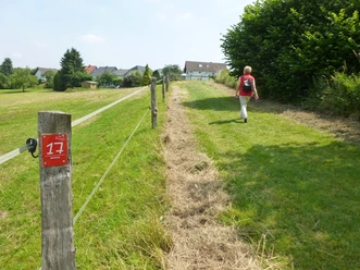 Wanderer auf dem Bierweg Eine Person wandert entlang eines Feldweg-Zauns mit einem roten Markierungsschild "17".