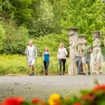 Kurpark Nümbrecht <p>Fünf Personen wandern in sommerlicher Kleidung durch einen grünen Park mit antiken Säulen.</p>